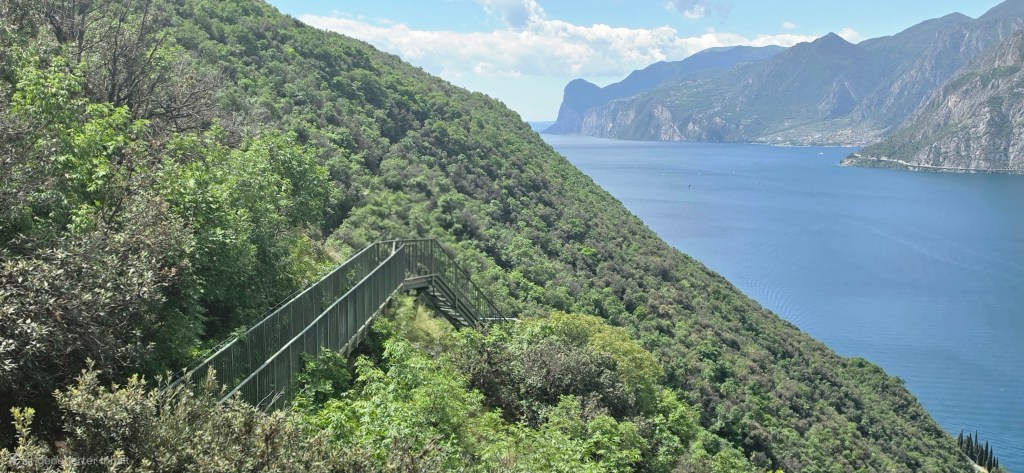 Aussicht vom Busatte-Tempesta Wanderweg am Gardasee mit Metalltreppe, grünen Berghängen, blauem Wasser und Panorama Richtung Süden.