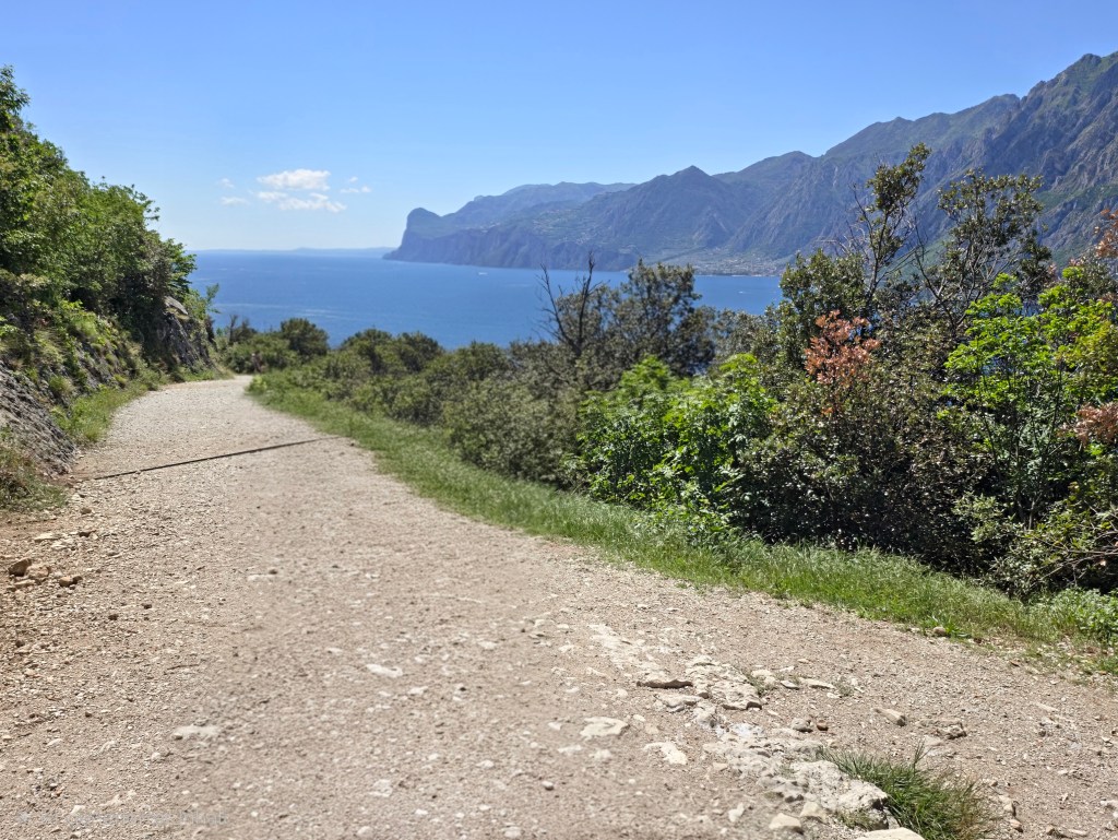 Panorama-Spot am oberen Weg des Busatte-Tempesta Wanderwegs oberhalb vom Gardasee mit Blick auf See, Berge und mediterrane Landschaft.