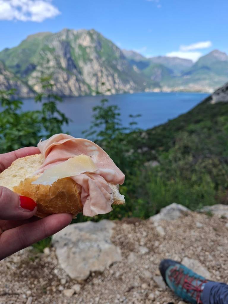 Wanderpause auf dem Busatte-Tempesta Wanderweg oberhalb vom Gardasee mit kleinem Snack, Seeblick, Bergen und entspannter Outdoor-Atmosphäre.